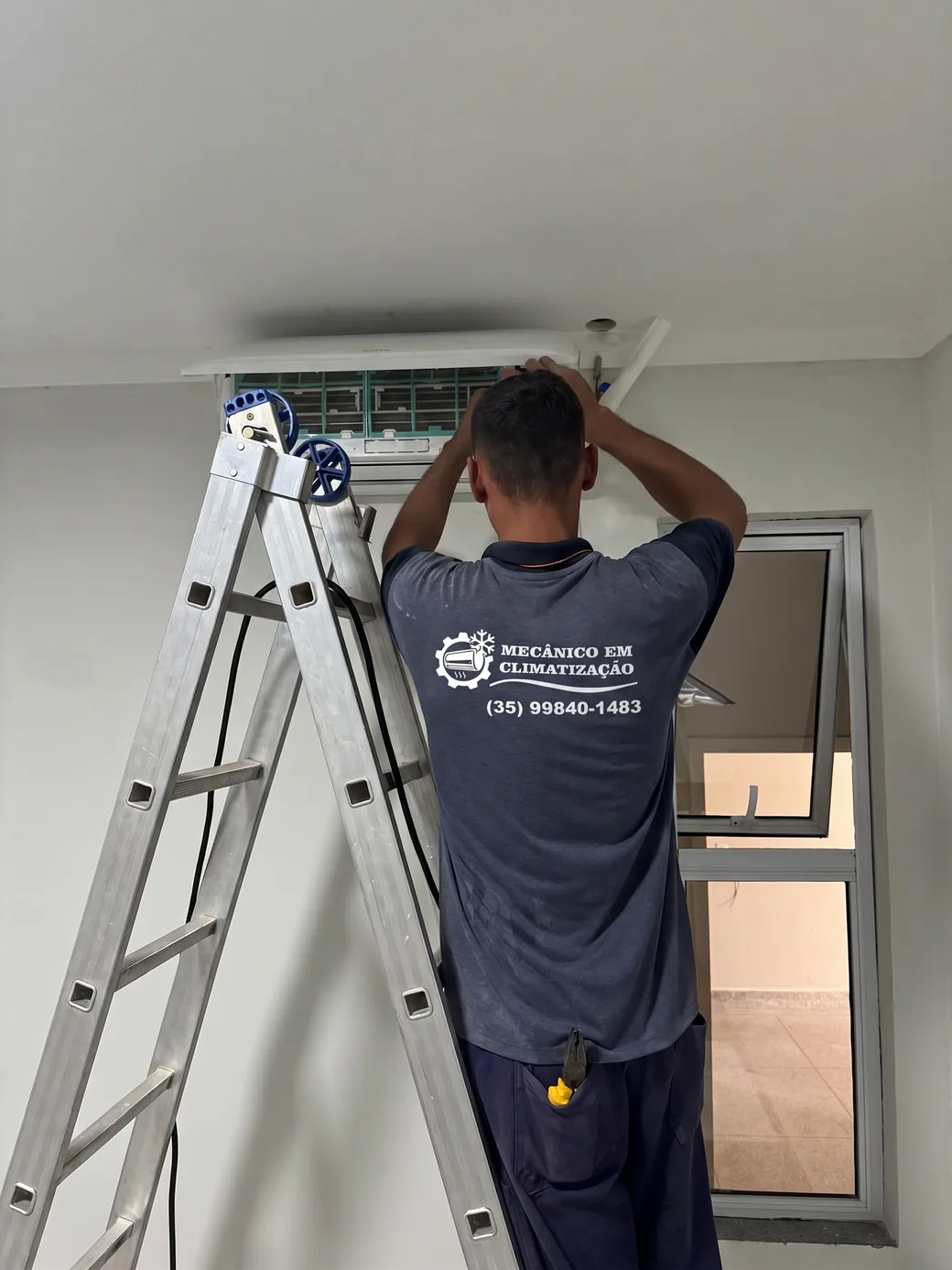 Técnico da Quality Service na escada, fazendo manutenção na unidade evaporadora de um ar condicionado